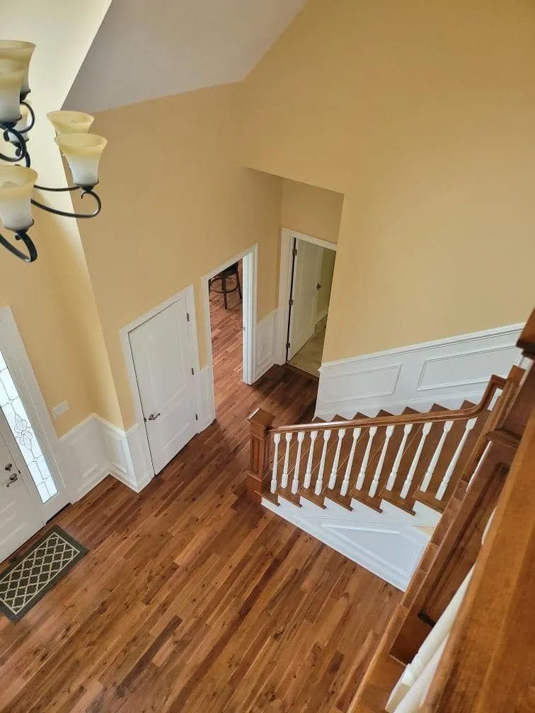 View of a two-story foyer with a staircase, hardwood floors, and cream-colored walls.