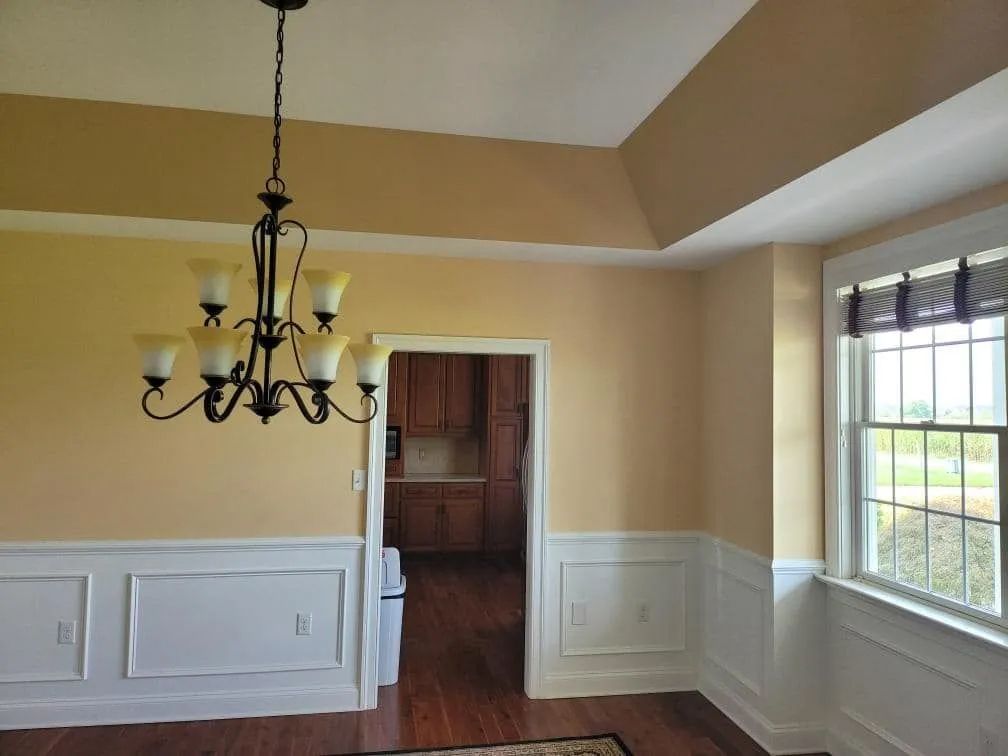 Dining room with tan walls, white trim, chandelier, and a view into the kitchen.