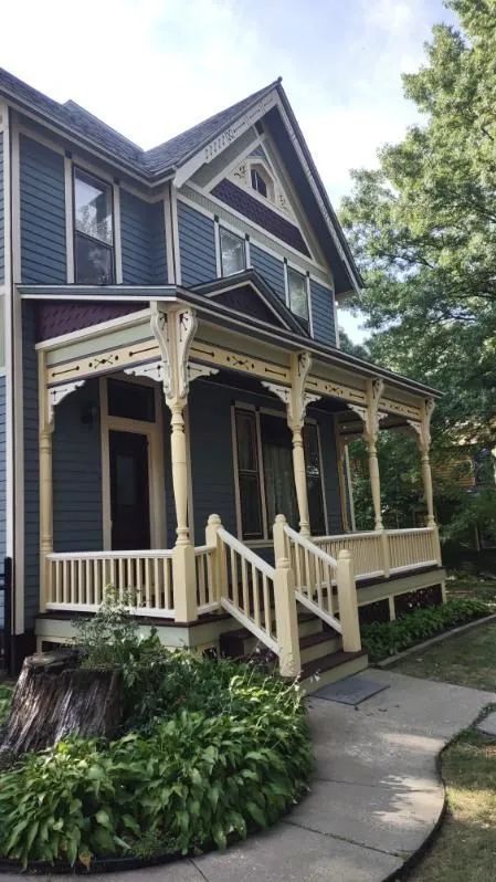 Two-story Victorian house with blue siding and beige porch, walkway, and landscaping.