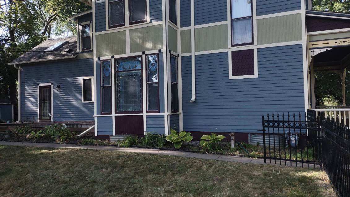 Blue Victorian house with green trim, a front lawn, and a black fence.