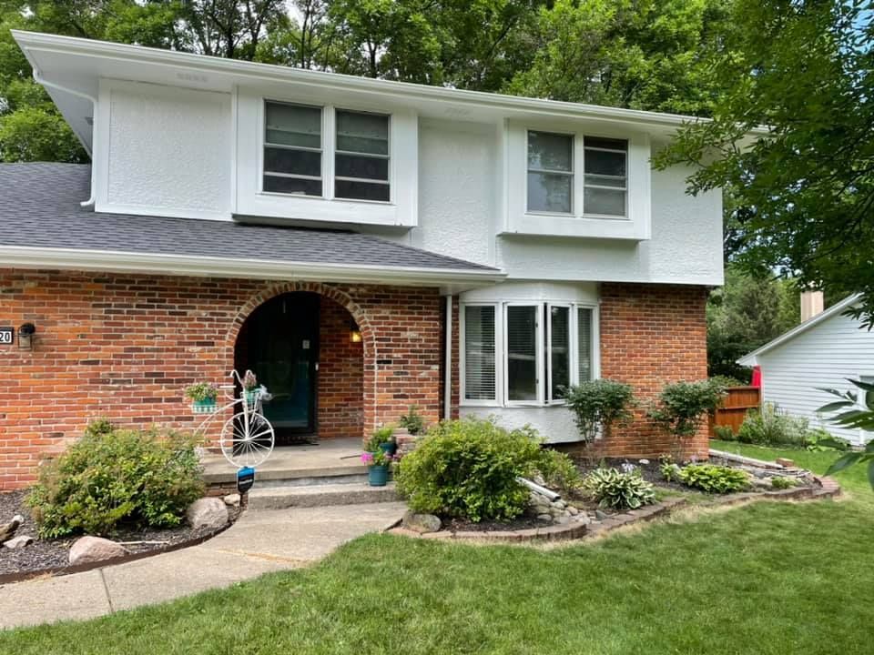 Two-story house with brick facade, white siding, and arched entryway. Lush green yard and landscaping.