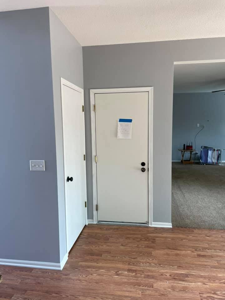 Entryway with wood-look floor, grey and white walls, two white doors. One has a paper taped to it.
