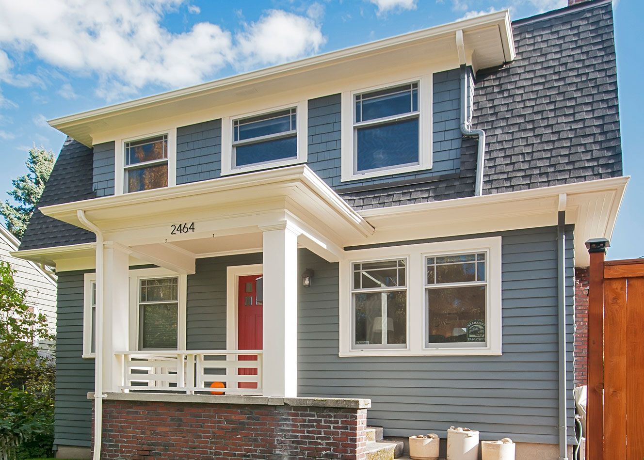 Blue two-story house with white trim and a red door, set against a blue sky.