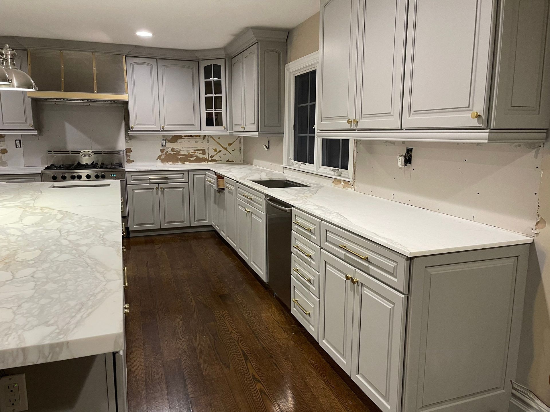 Kitchen undergoing renovation with gray cabinets, white countertops, and exposed walls.