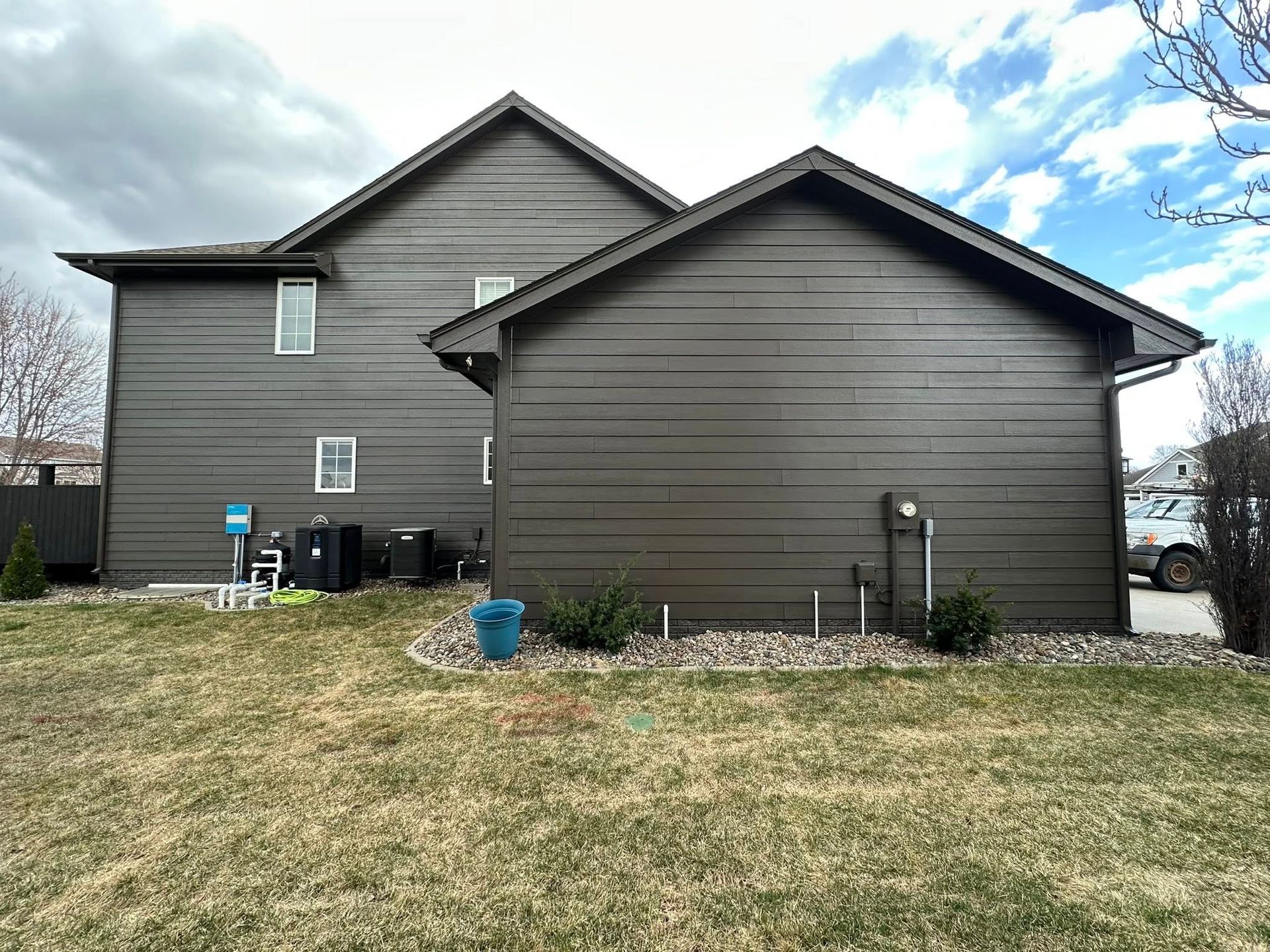 Brown house with a garage, on a grassy lawn under a cloudy sky.