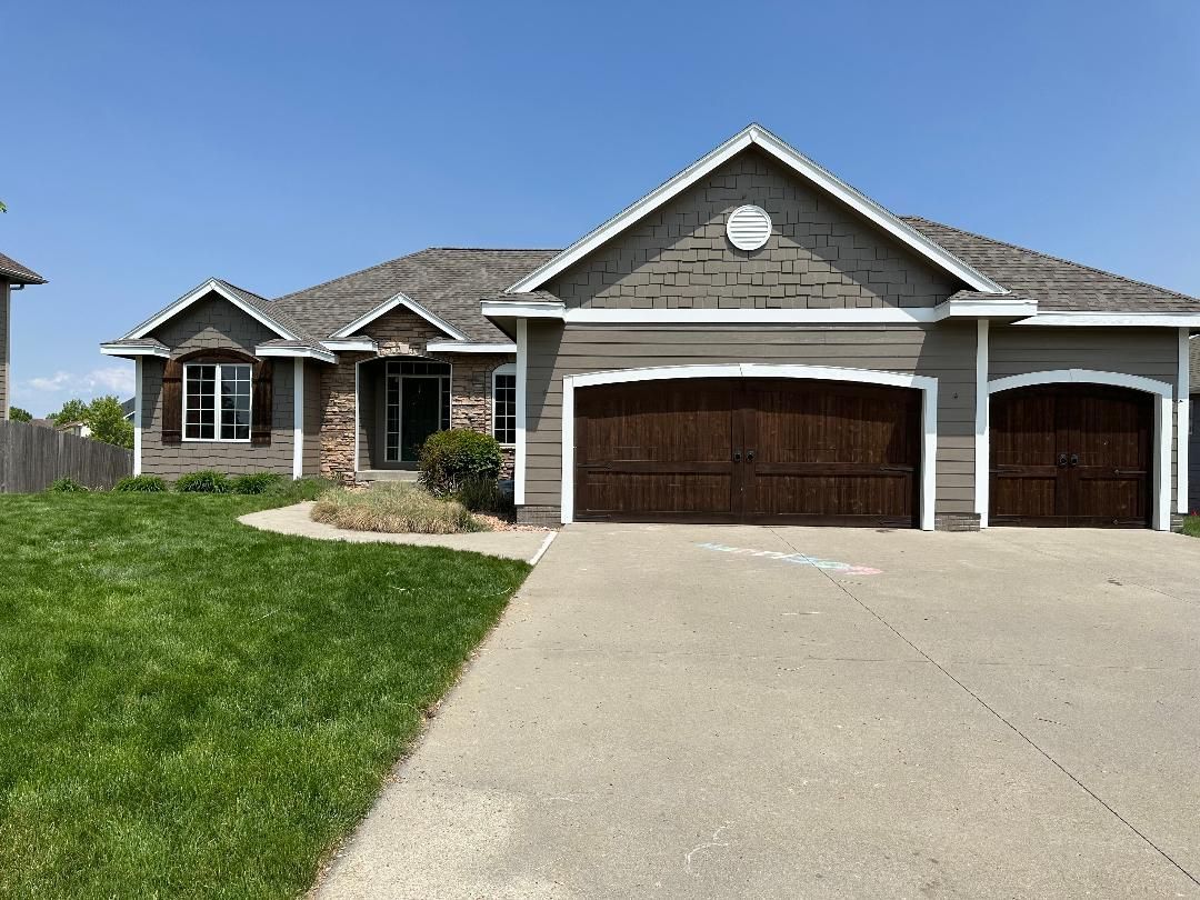 A one-story house with a brown garage door and a paved driveway, under a clear blue sky.