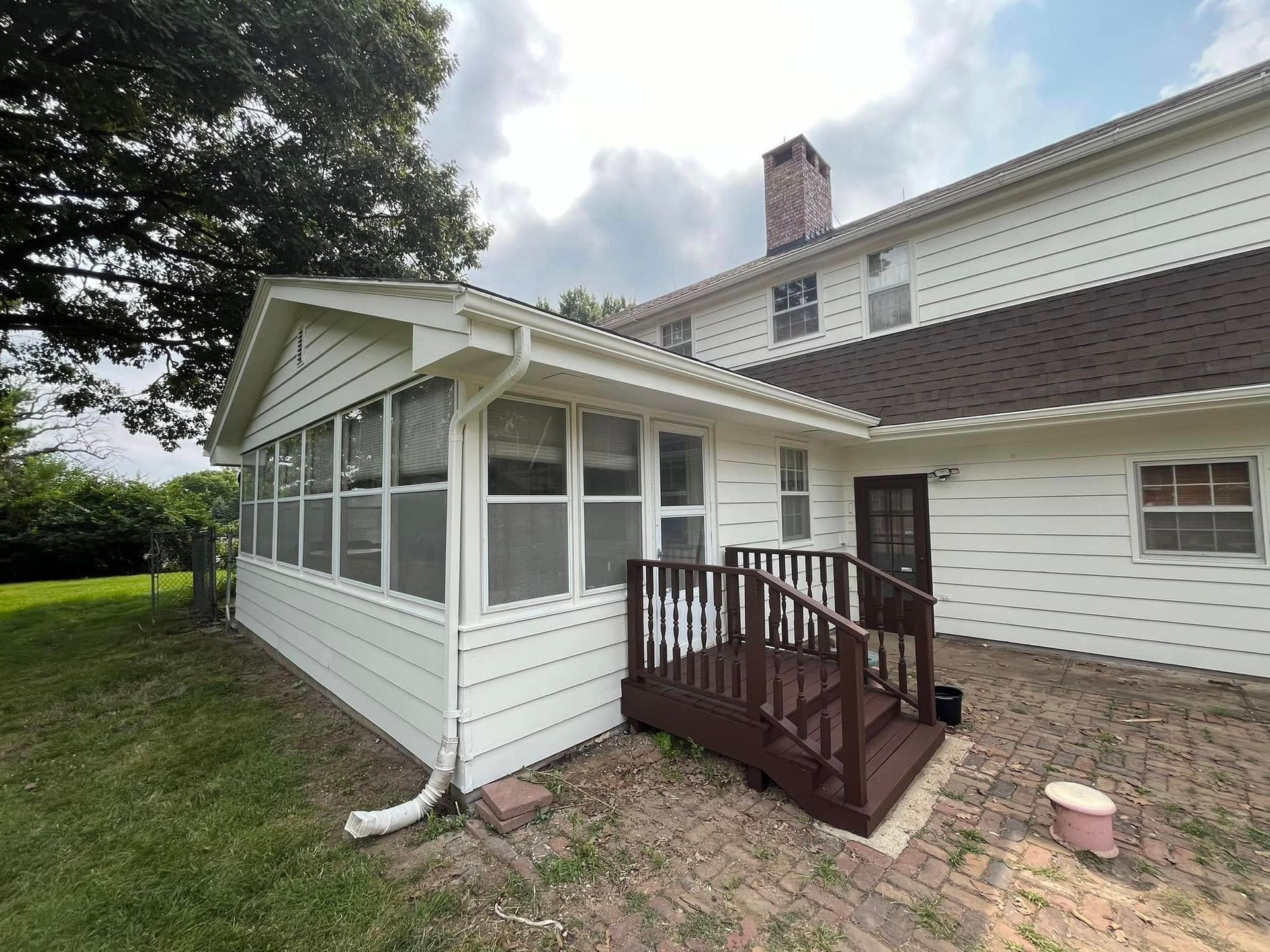 White house with screened porch and wooden deck; brown roof and brick patio.