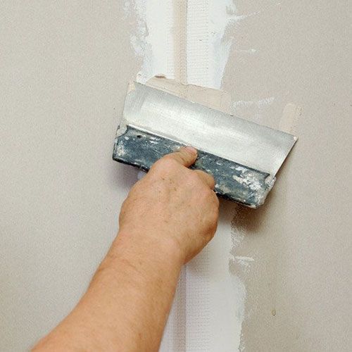 Person using a putty knife to apply joint compound on a drywall seam.