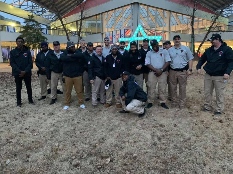 A group of men in security uniforms posing outdoors in front of a building with a star decoration.