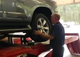 Mechanic working on a green SUV on a red lift in a garage