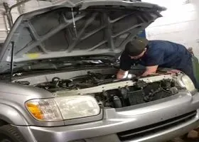 Mechanic inspecting a silver car’s engine with the hood open in a garage