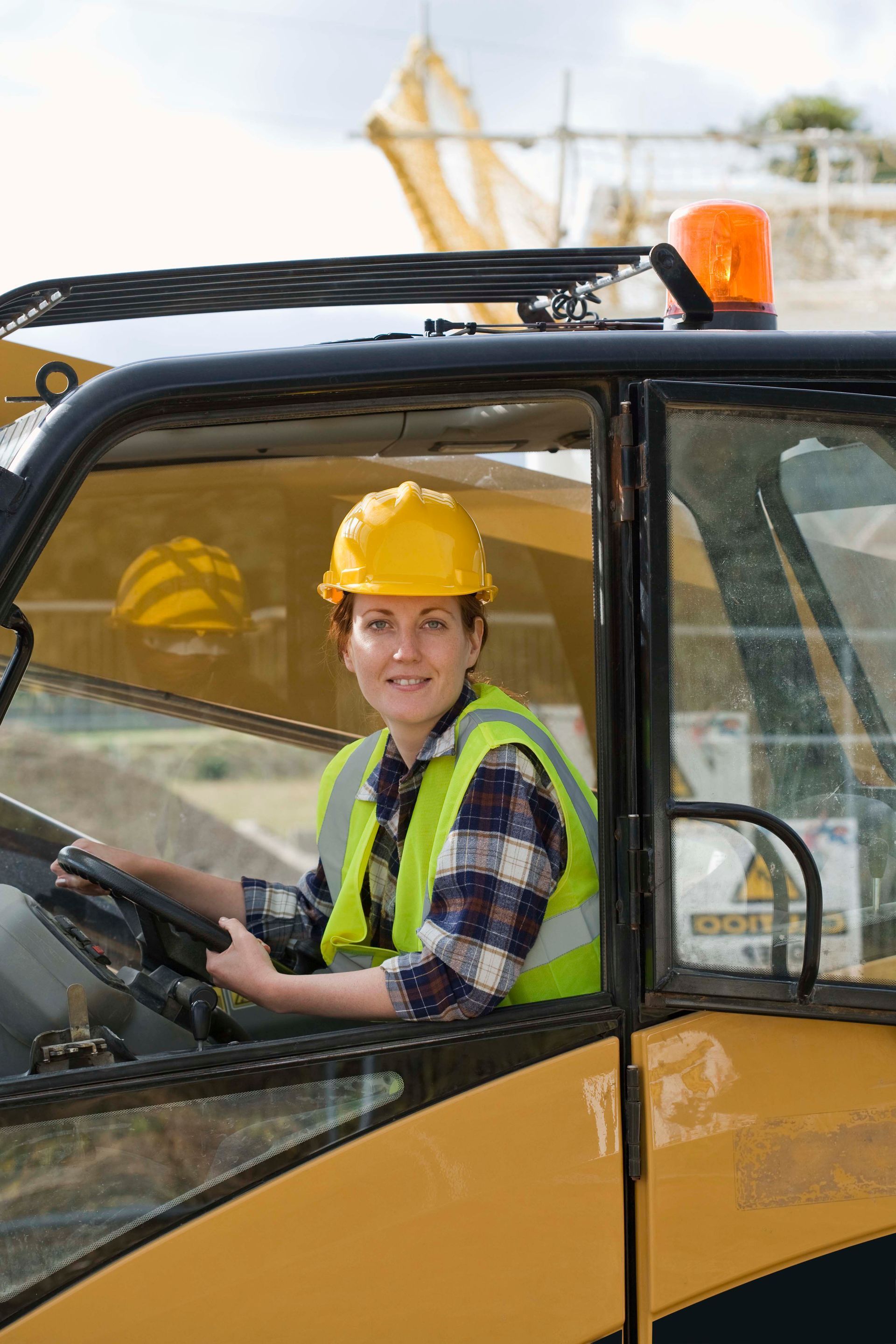 Woman in yellow hard hat and vest driving construction equipment.