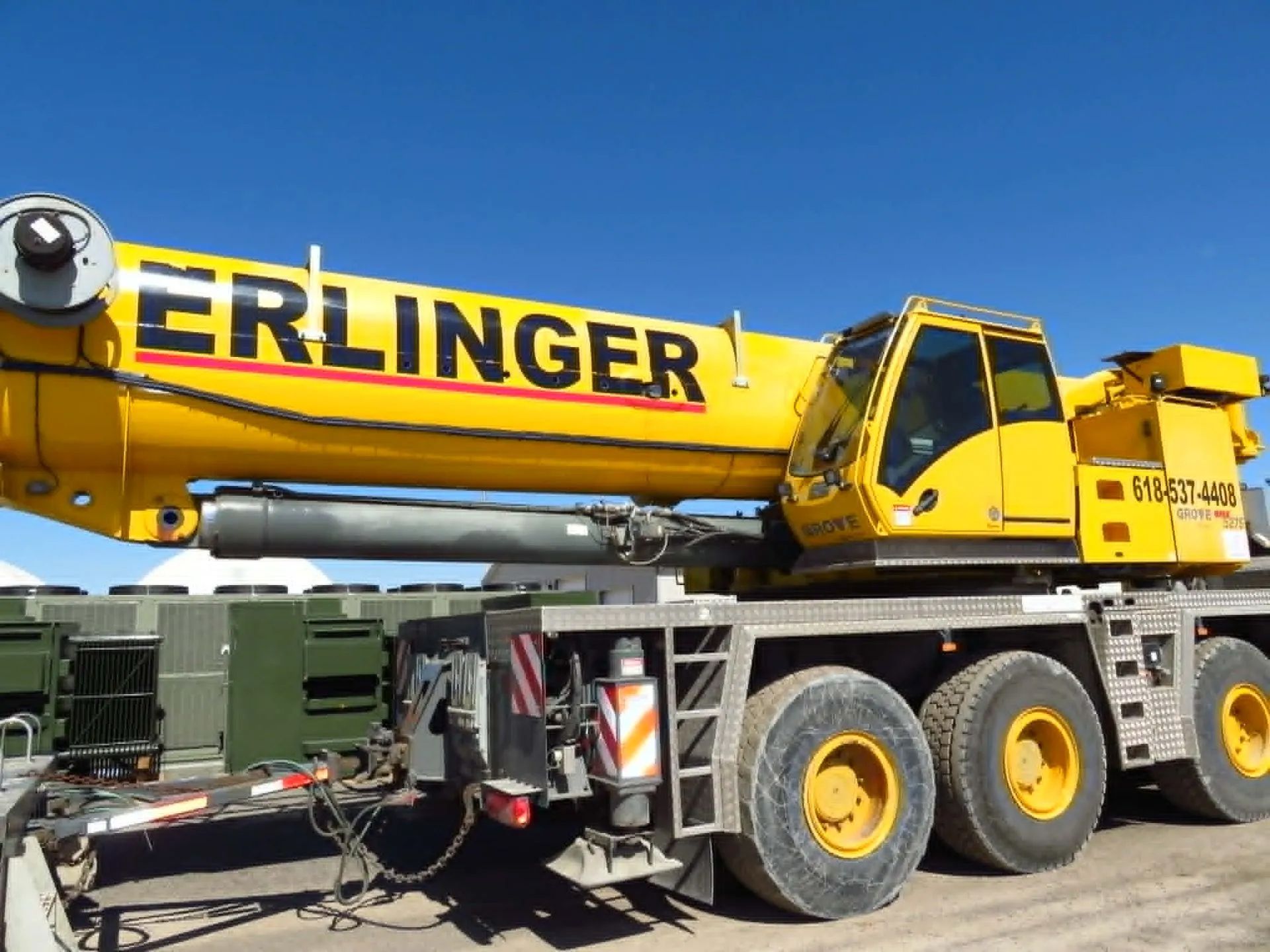 Yellow Erlinger crane on a truck with black tires against a clear blue sky.
