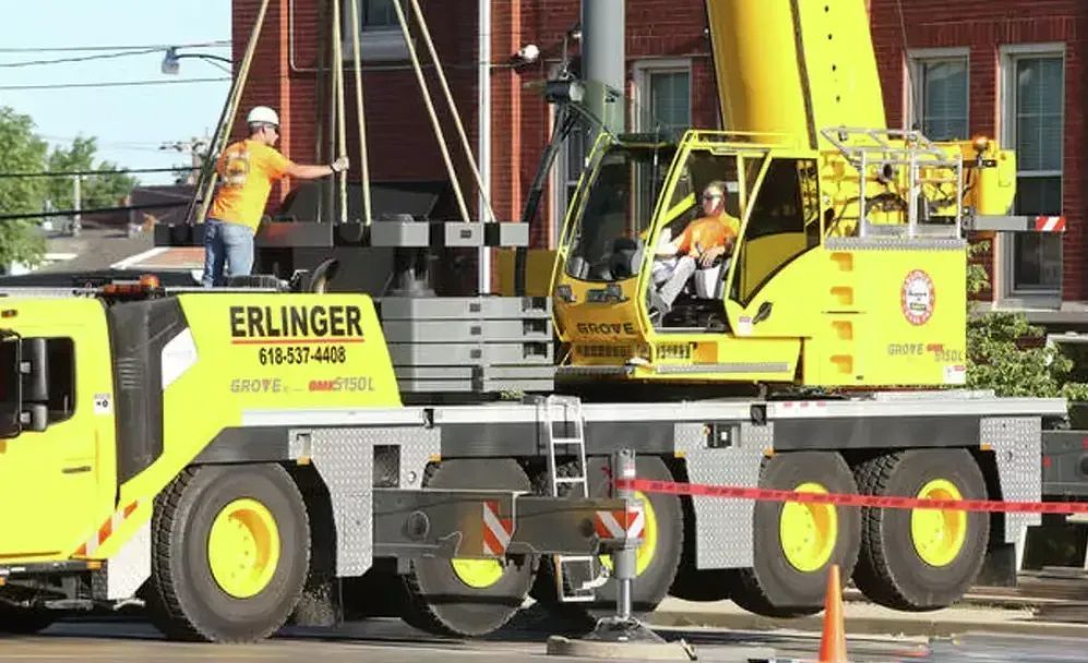 Yellow crane at a construction site; workers in orange shirts.