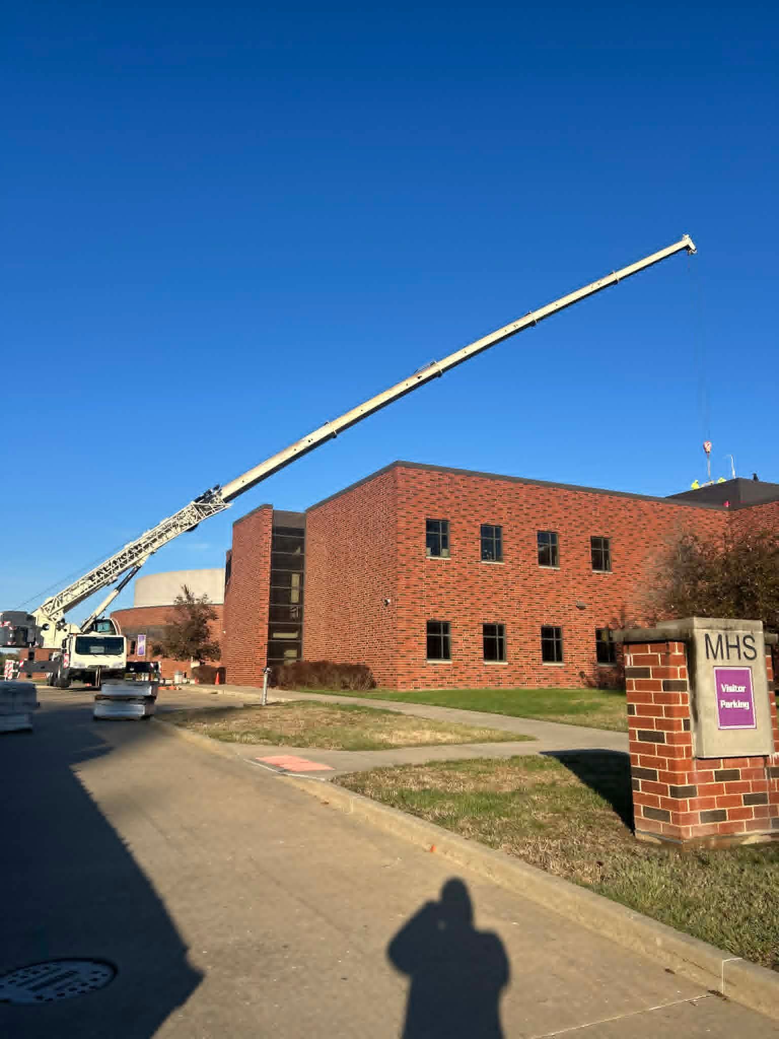 A cherry picker extended towards a brick school building on a sunny day. WHS sign on right.