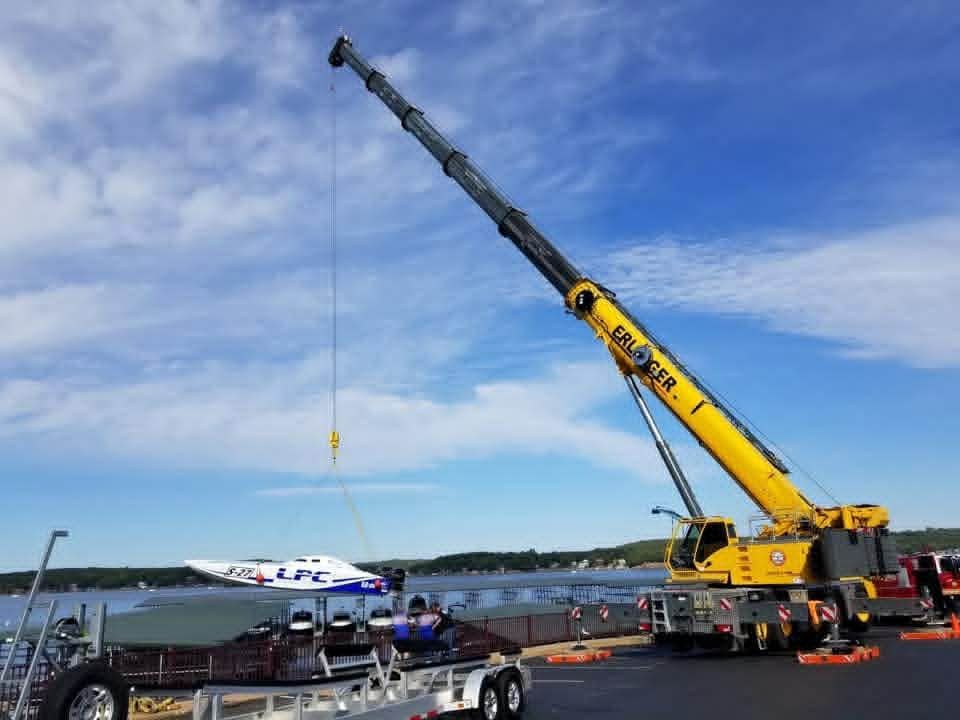 Yellow crane lifting a boat on a trailer, blue sky in background.