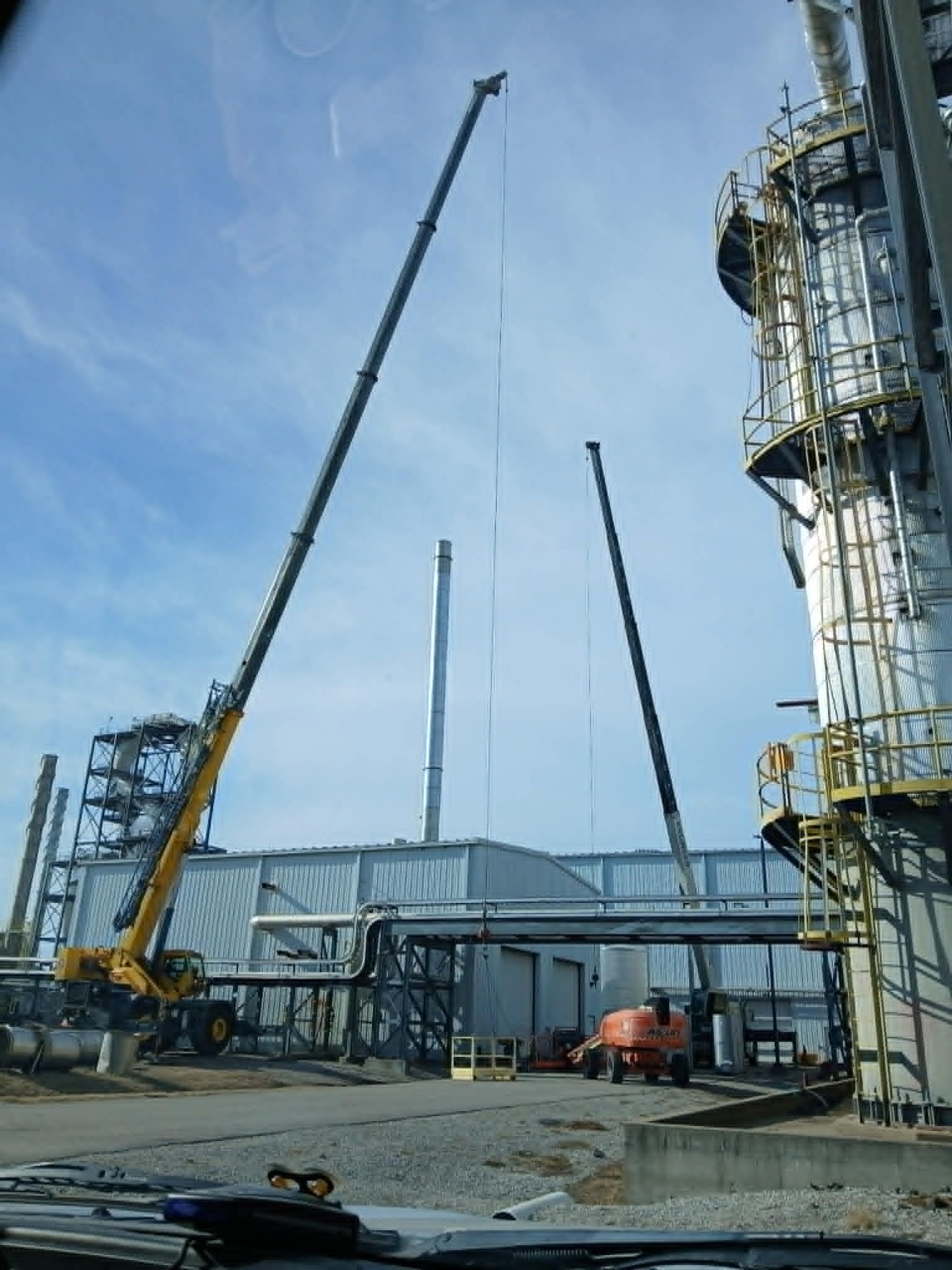 Two cranes working on industrial equipment against a cloudy sky.
