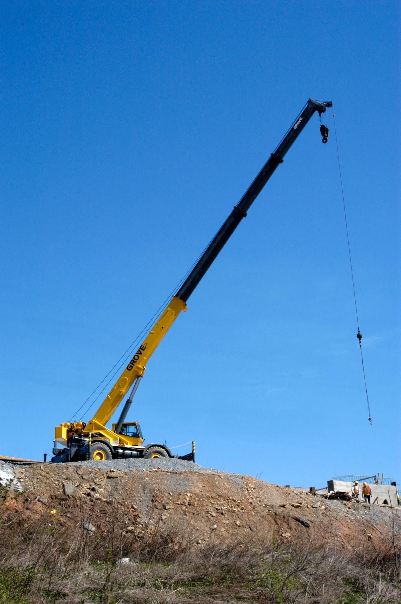 Yellow crane on a rocky hill lifting a load against a clear blue sky
