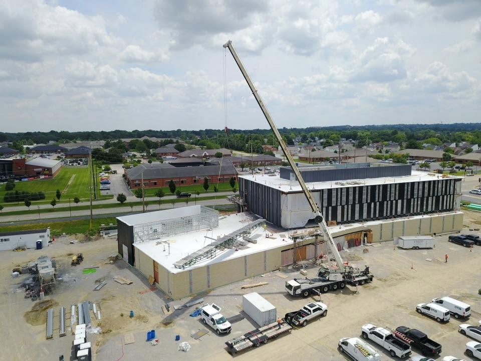 Construction site with crane beside a partially built building and parked vehicles under cloudy skies