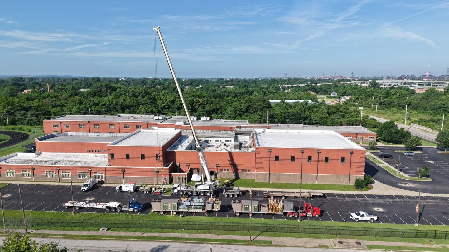 Aerial view of a brick building under construction with a crane, surrounded by roads and green trees.
