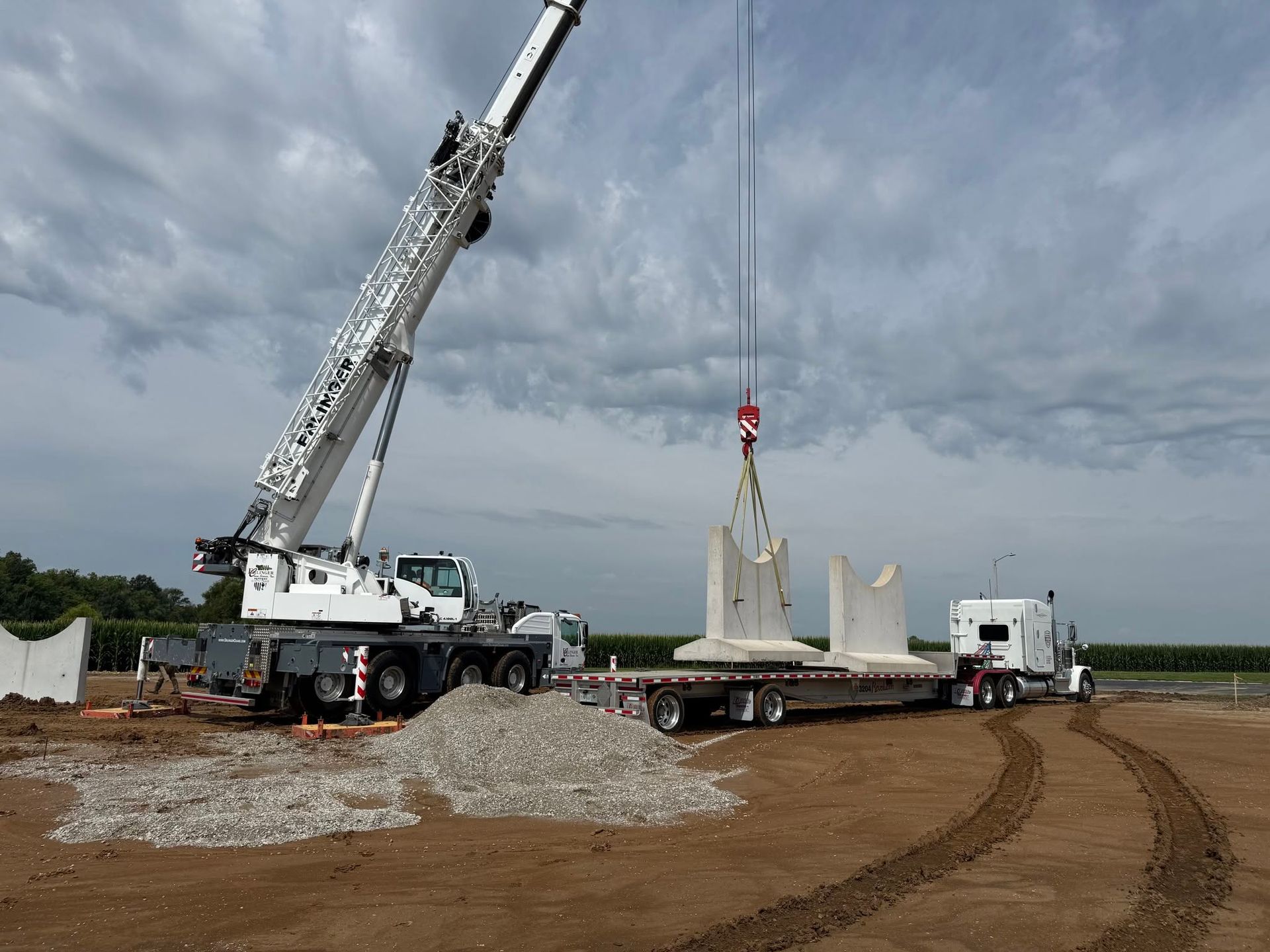 Crane lifting a concrete wall panel at a construction site under cloudy skies