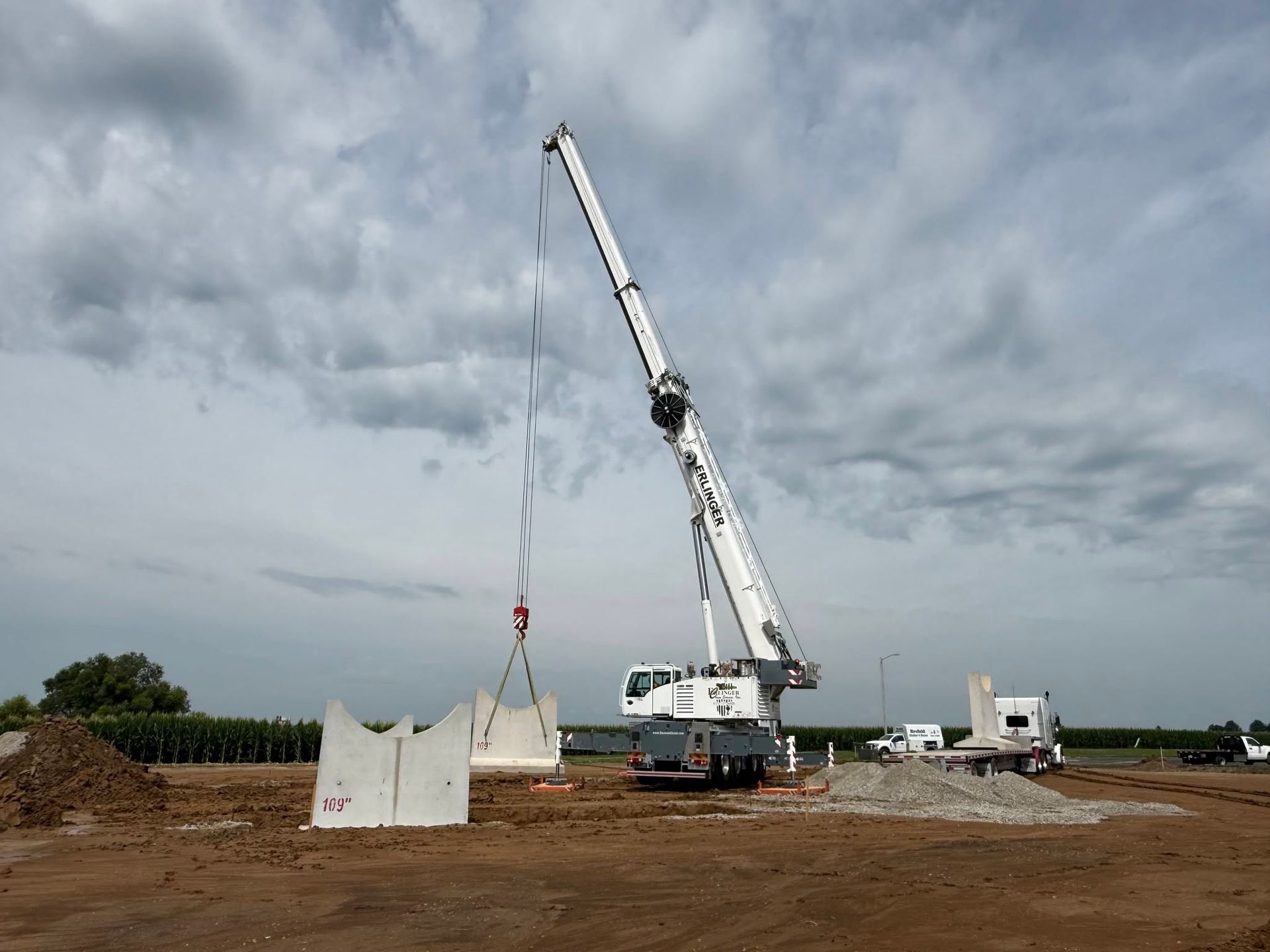 Construction site with a white crane lifting a concrete panel under a cloudy sky
