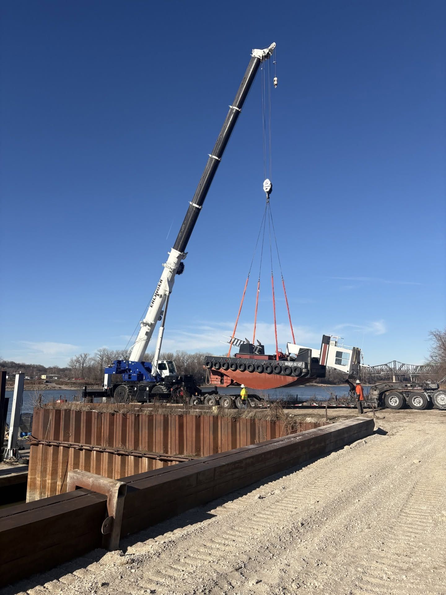 Crane lifting a large steel structure at a construction site under a clear blue sky