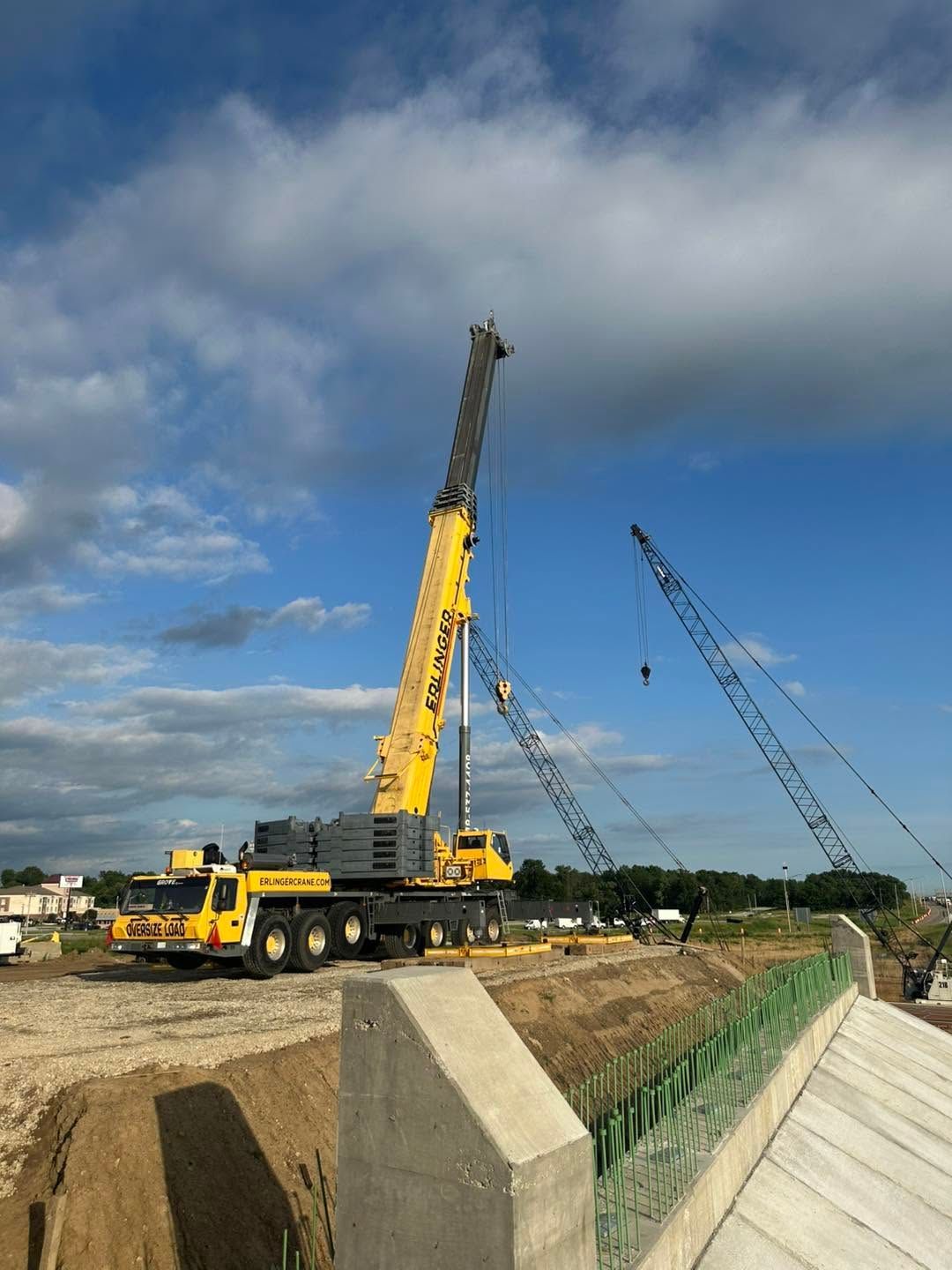 Yellow crane truck lifting on a construction site beside a canal under a cloudy sky