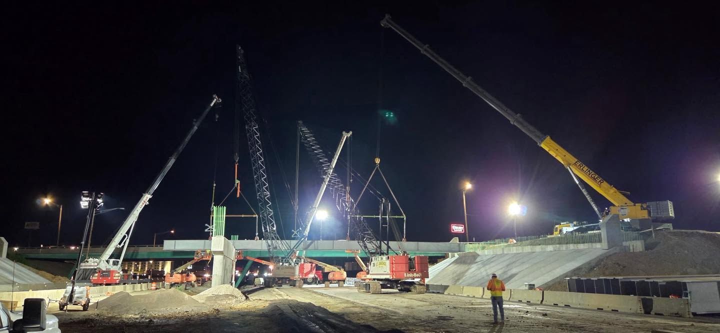 Nighttime construction site with cranes, heavy machinery, and bright floodlights
