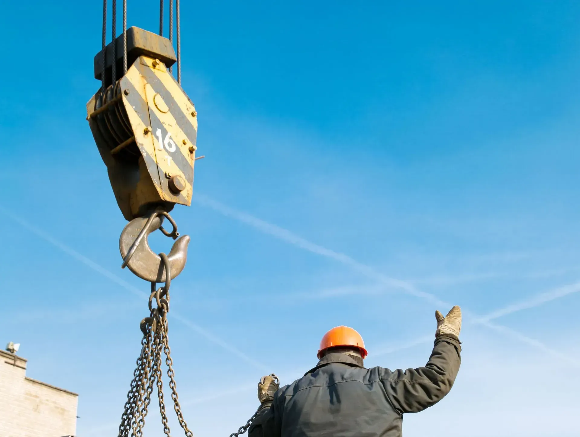 Construction worker guiding a crane hook, blue sky background.