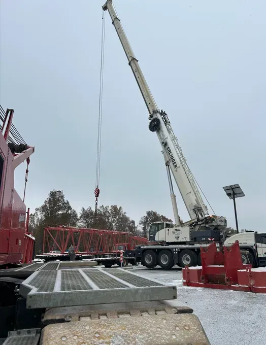 Crane lifting a red metal structure on a snowy day. A large red truck is in the foreground.
