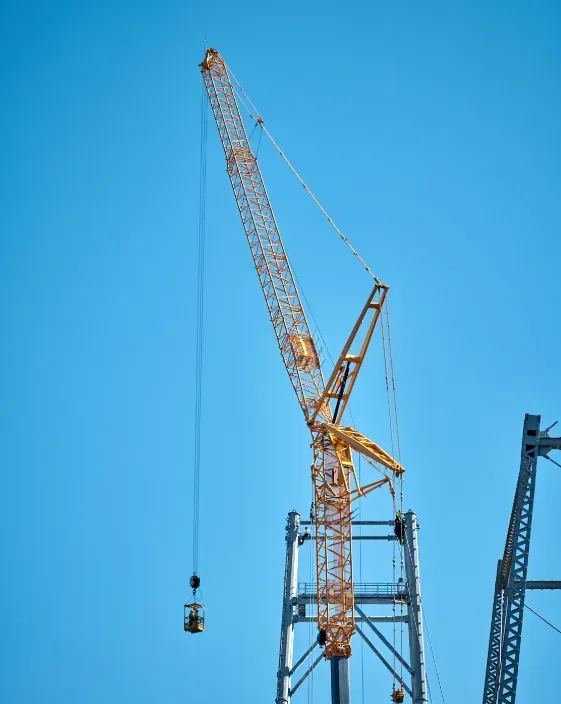 Yellow construction crane against a bright blue sky, holding a small basket.