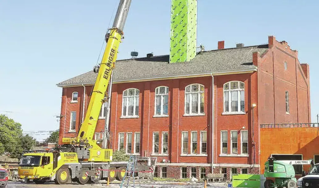 A yellow crane lifting a green structure onto a red brick building under construction.