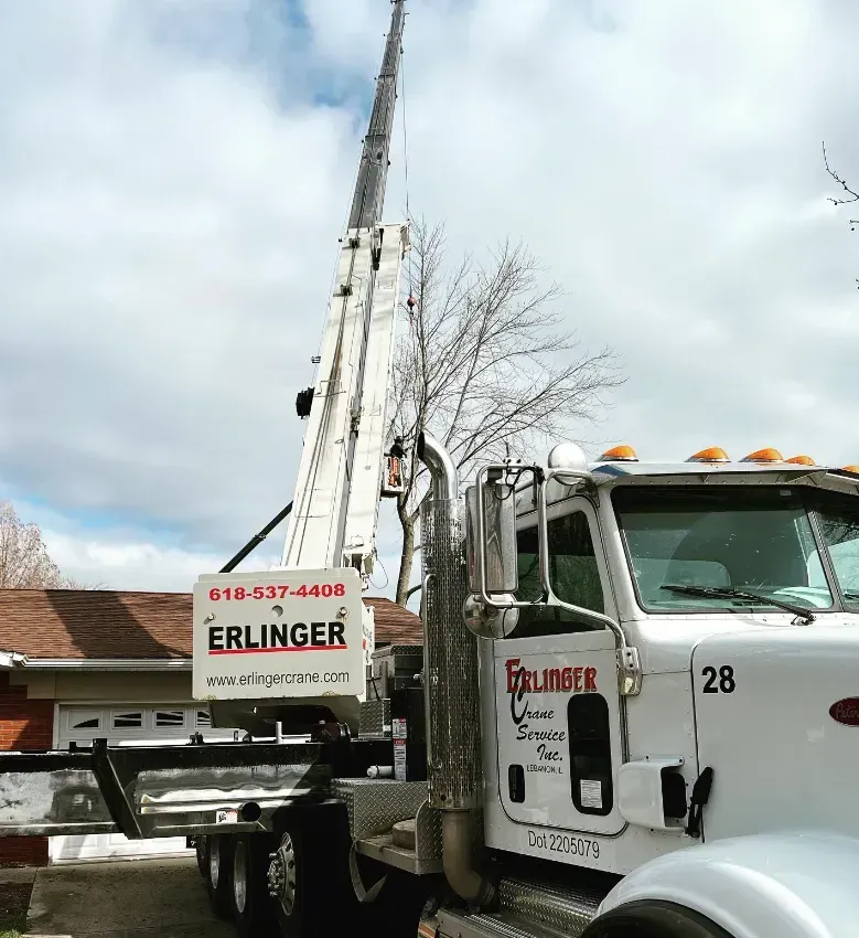 A white Erlinger truck with a crane assisting a residential roof.