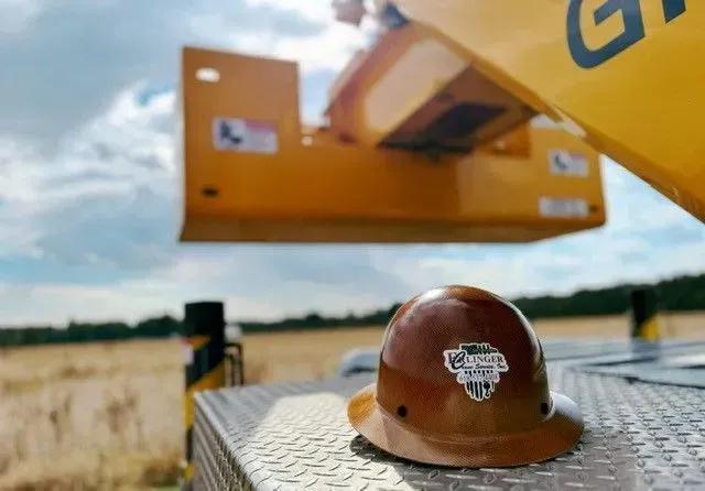Brown hard hat on a truck bed, with a yellow arm holding equipment overhead, outdoors.