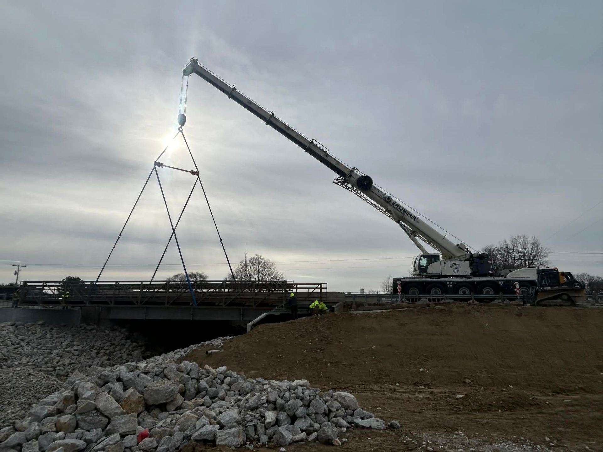 Crane lifting a bridge section during construction near a cloudy sky.