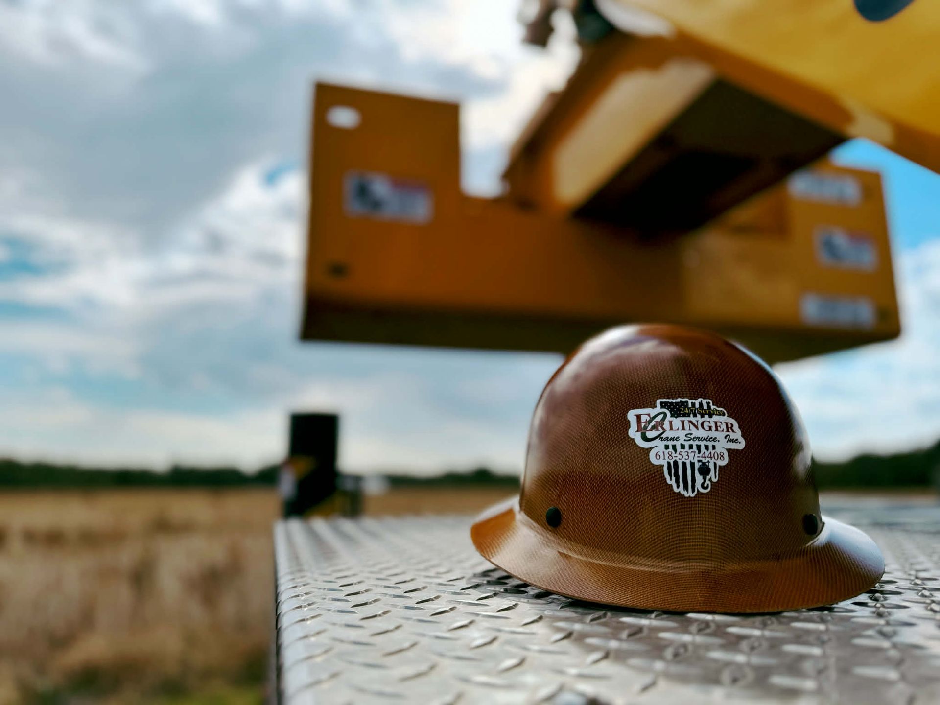 Brown hard hat with sticker on a metal surface, crane in background.
