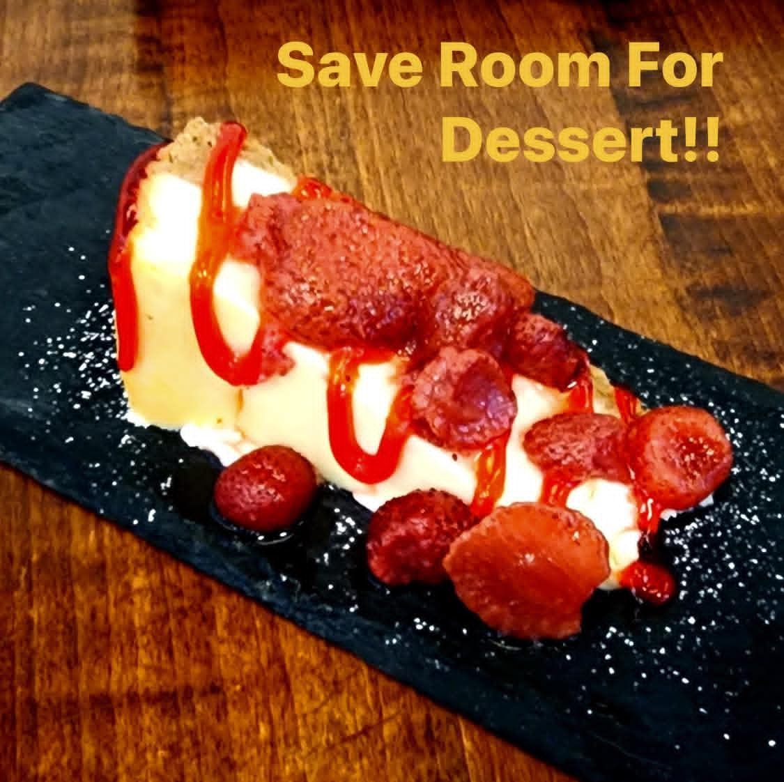 Slice of cheesecake with strawberry topping on a black slate, on a wooden table, with text