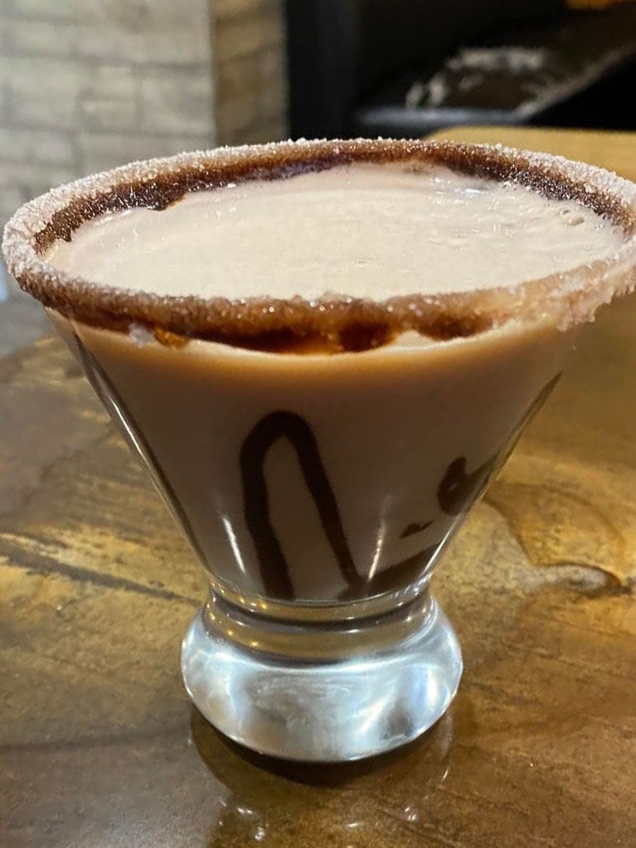 Chocolate martini with sugar rim and chocolate drizzle in a stem glass on a wood surface.