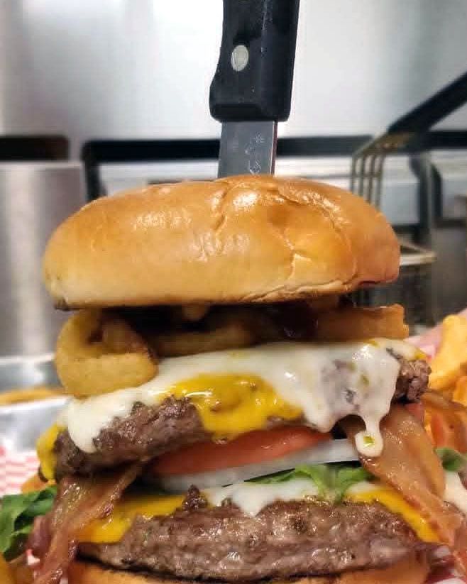 Double-decker burger with cheese, bacon, onion rings, and a knife holding it together.