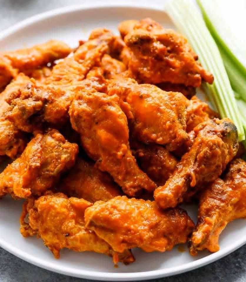 Buffalo wings on a white plate with celery sticks; wings are orange and coated in sauce.