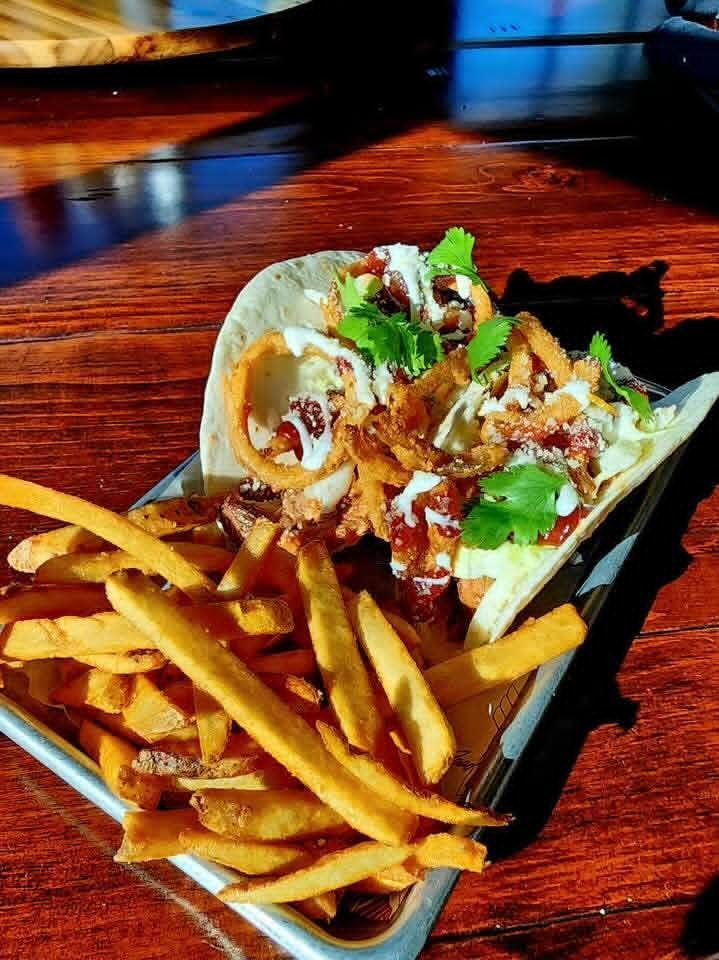 Taco with fries on a tray. Taco with onion rings, sauce, and cilantro; fries golden brown.