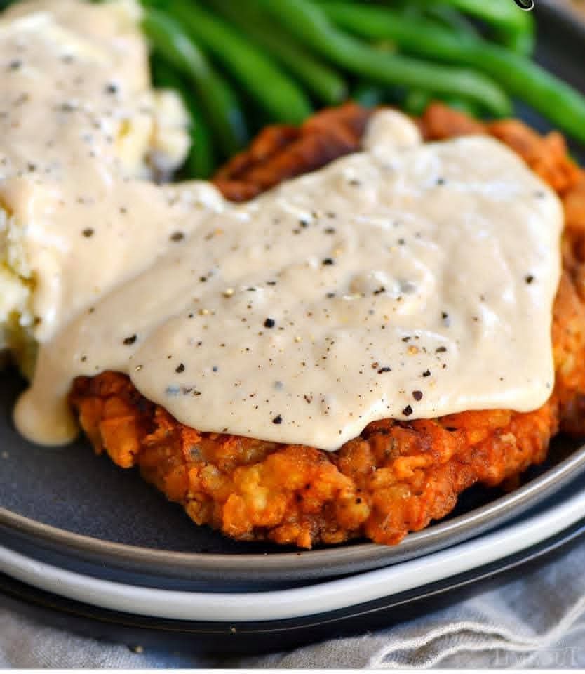 Chicken fried steak covered in gravy, served with mashed potatoes and green beans.