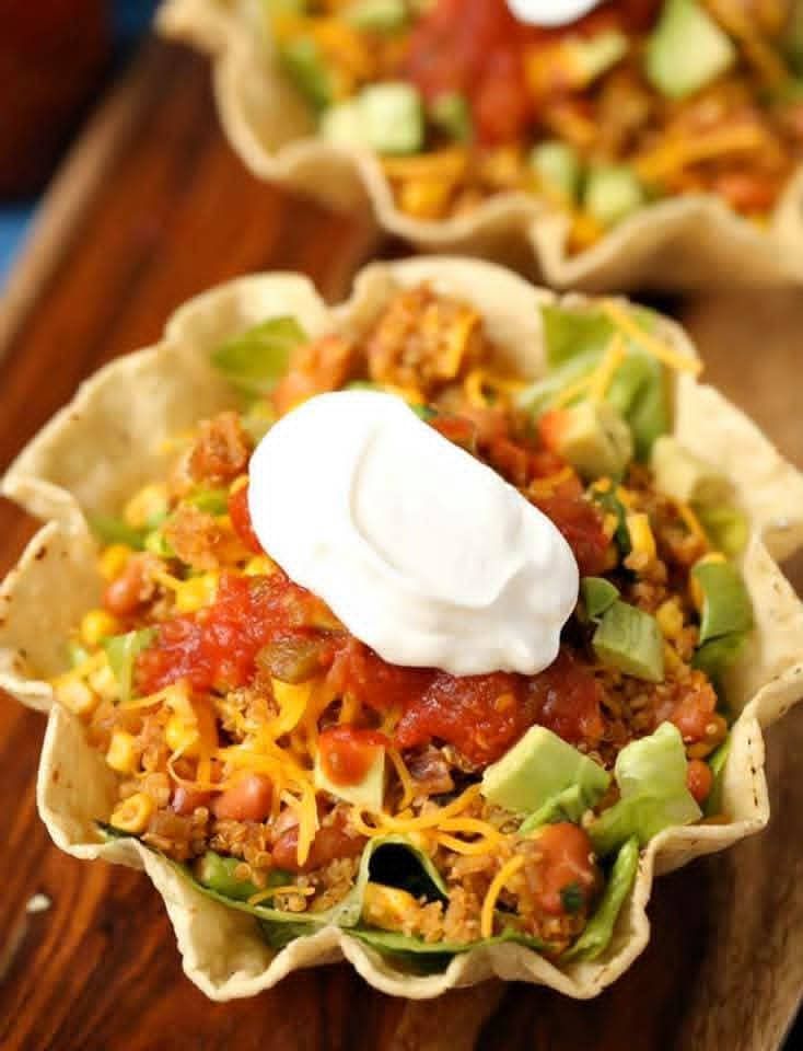 Taco salad in a crispy tortilla bowl, topped with sour cream, salsa, avocado, and cheese.