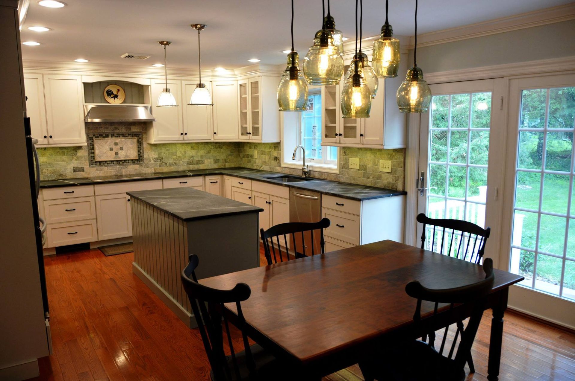 Kitchen with white cabinets, island, and dining table; hardwood floors and French doors.