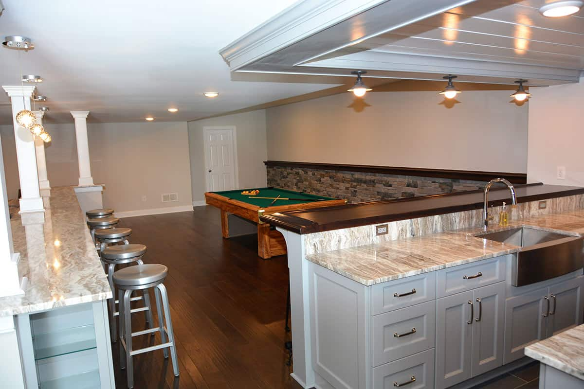 Basement entertainment area with a bar, pool table, dark wood floors, and grey cabinets.