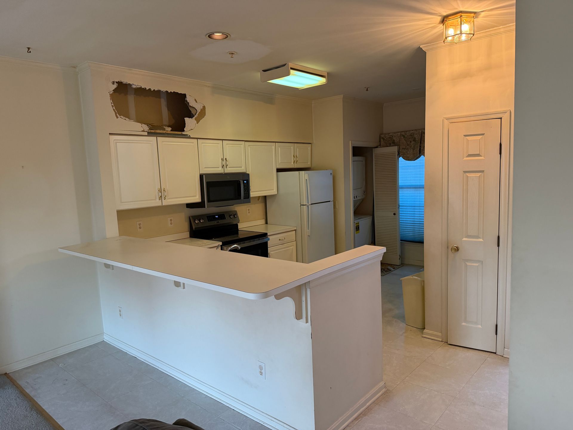 Empty kitchen with white cabinets, a breakfast bar, and a view into a blue bedroom doorway.