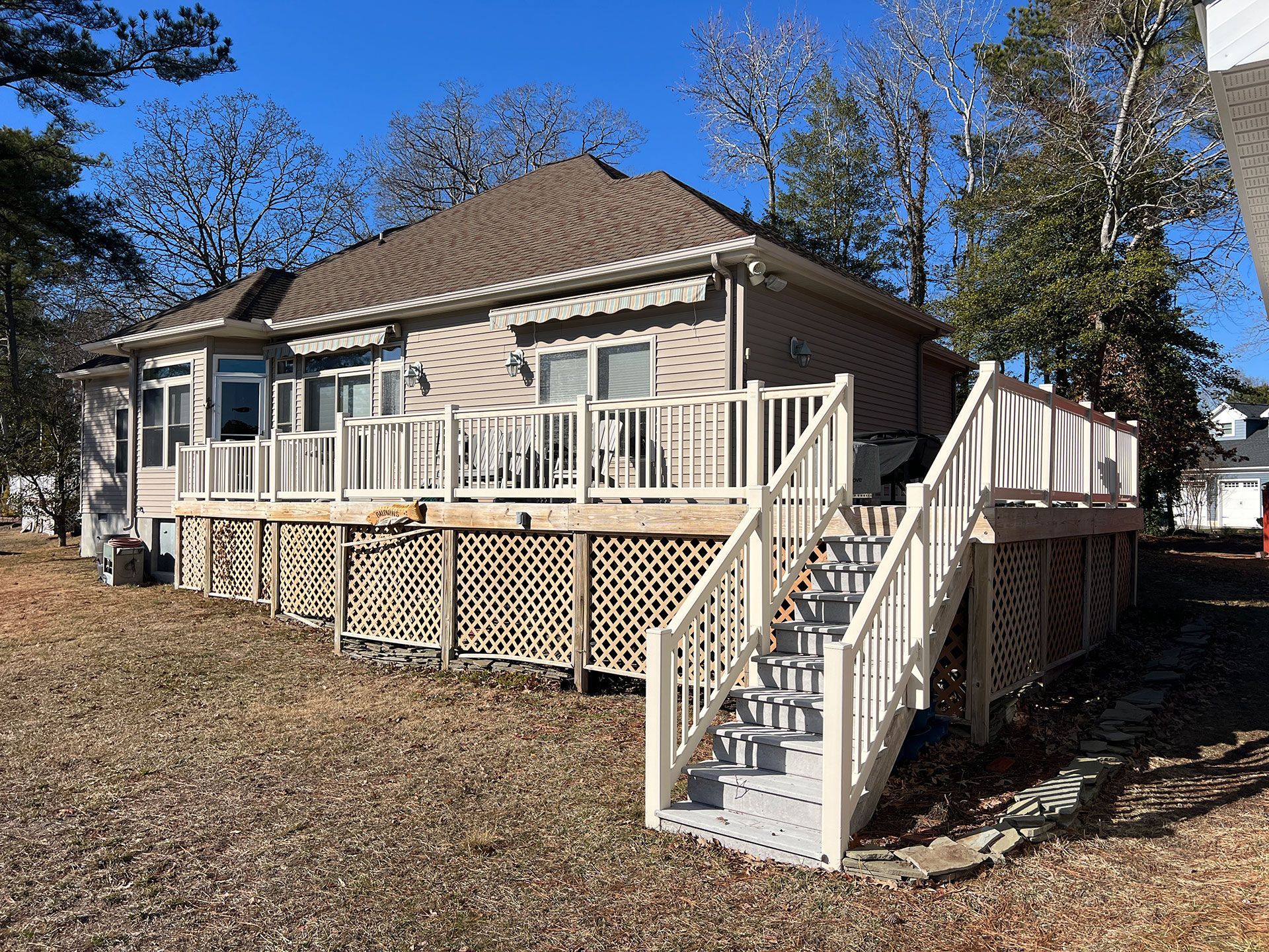 Back view of a house with a large deck, stairs, and lattice skirting in a grassy yard on a sunny day.