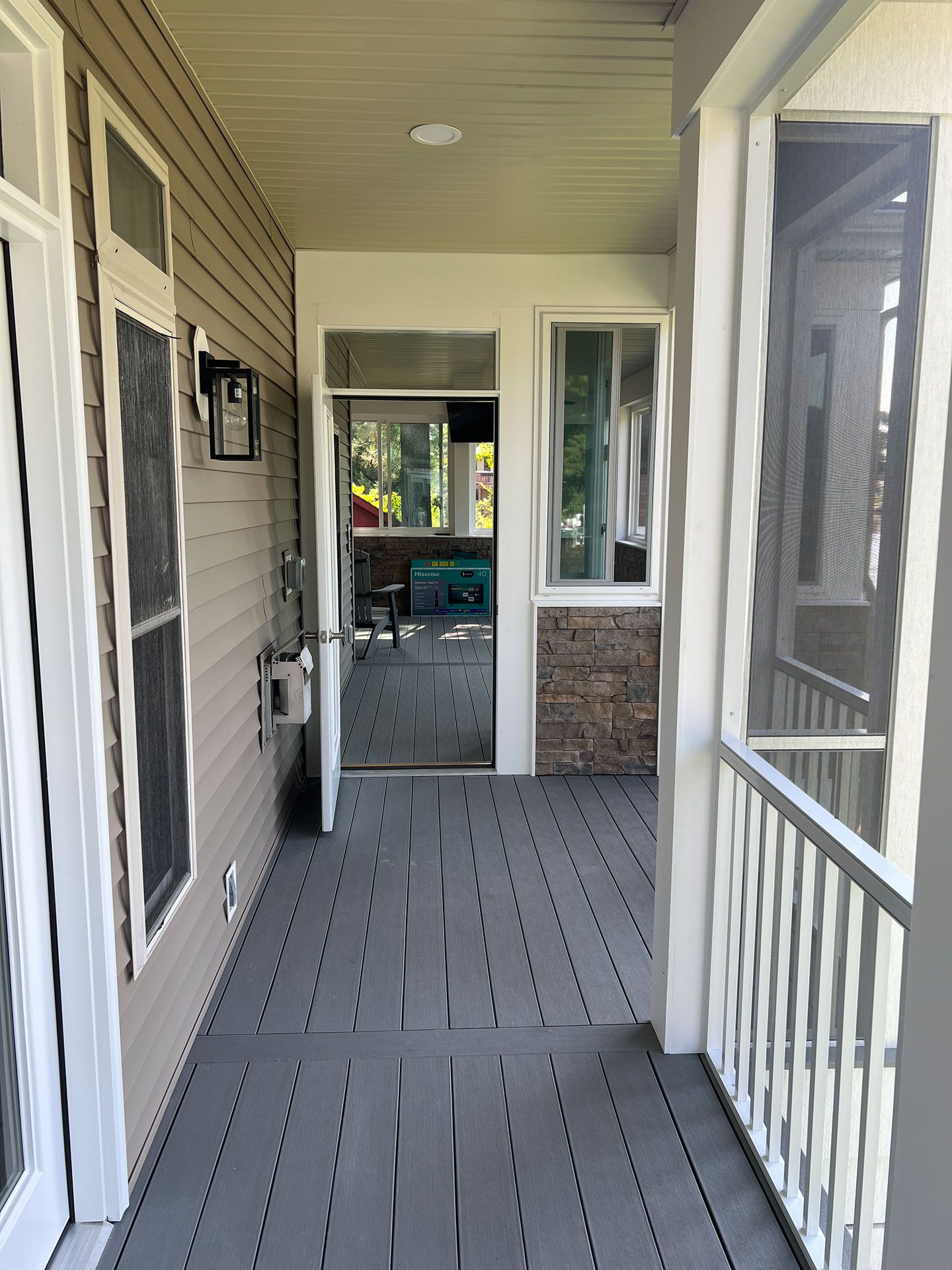 A covered porch with a gray deck, a screen door, and a white railing.