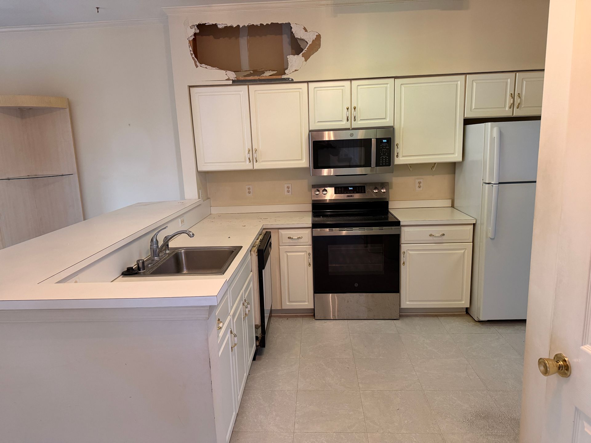 Small white kitchen with stove, refrigerator, sink, and missing upper cabinet panel above the counter.